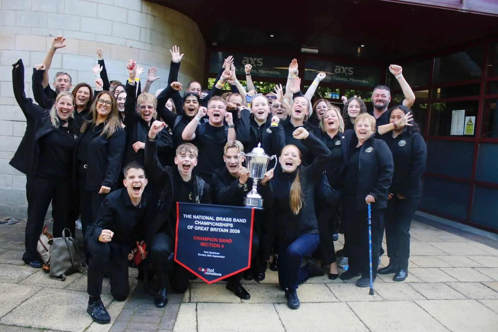 Wardle Community Band players, aged from teenagers to pensioners, cheering outside York Barbican with the National Championships trophy and a Section 4 Champion Band pennant